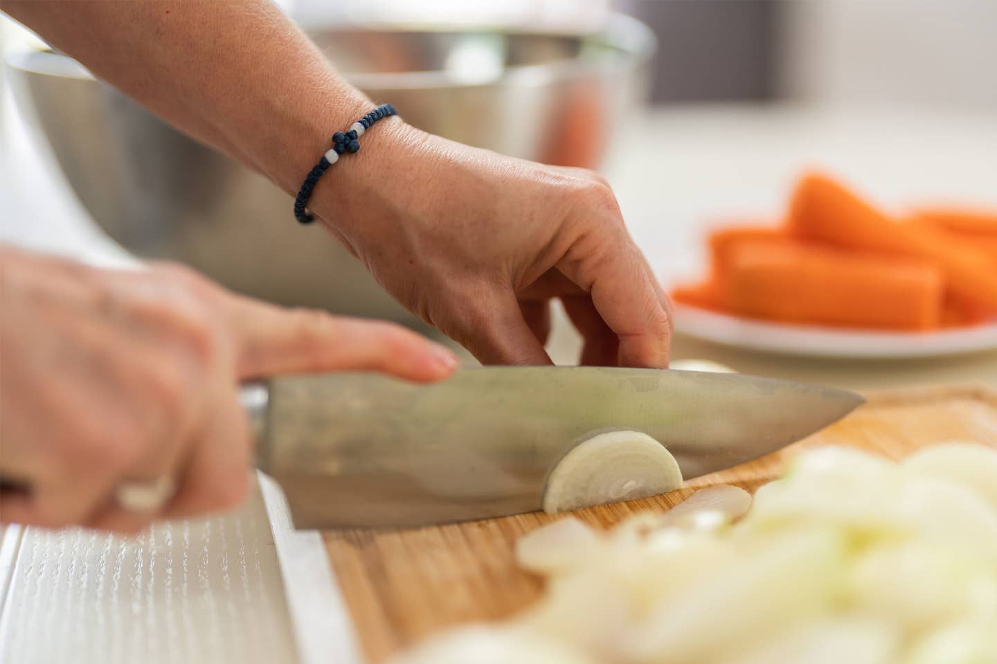 Woman making mirepoix unidentified hands making mirepoix, cutting onion on a chopping board with a plate of carrots in the background