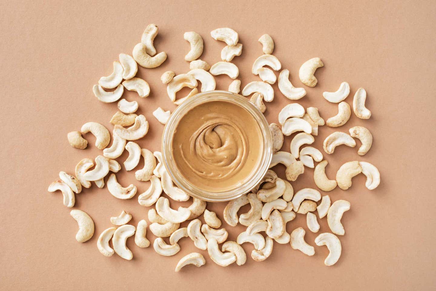 A jar of creamy cashew butter surrounded by raw cashews