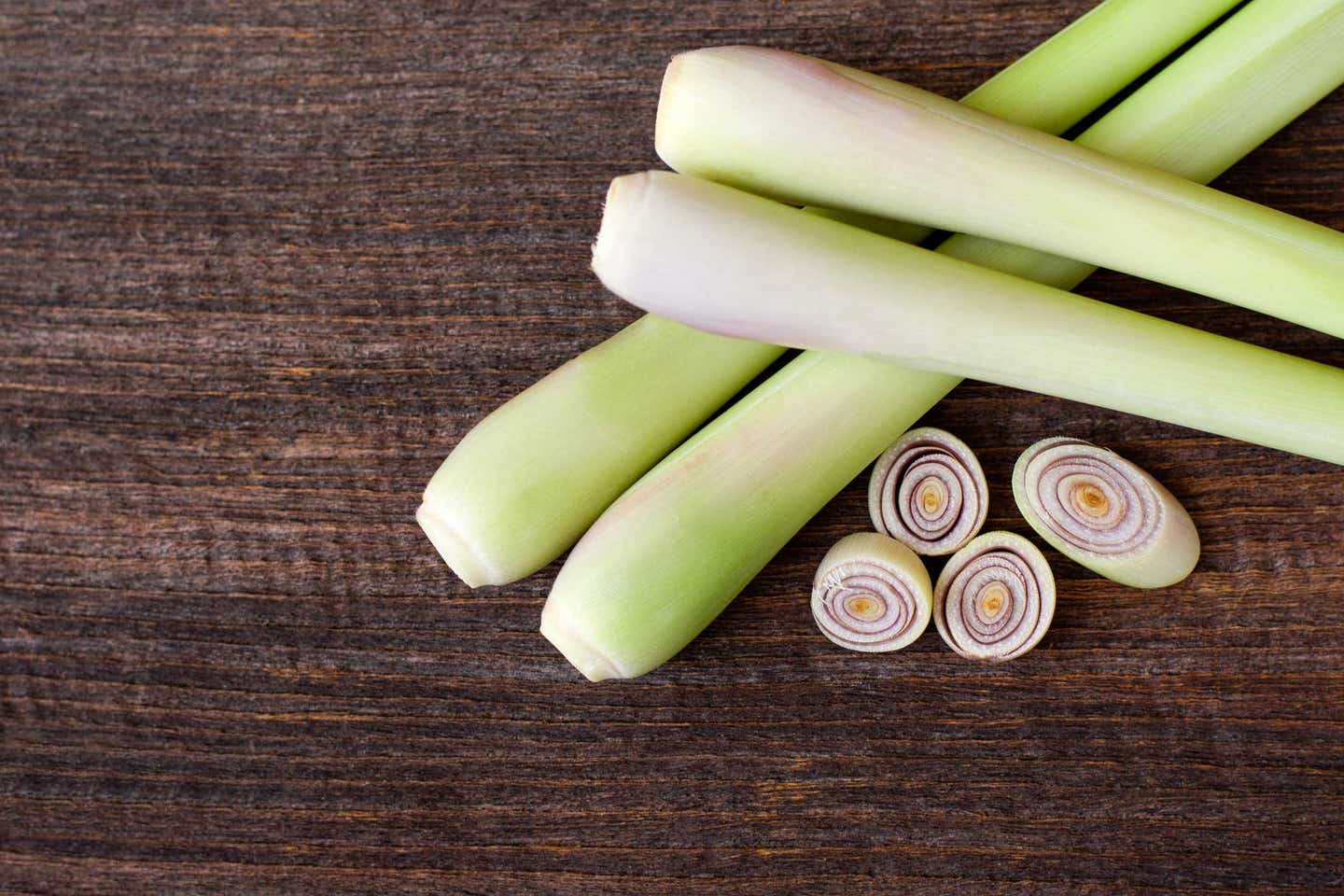 lemongrass-IQ Four stalks of lemongrass shown close up, with a few rounds of sliced lemongrass lying beside them